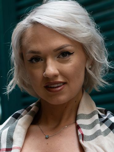 Close-up portrait of a blonde woman with winged eyeliner and a plaid shawl.