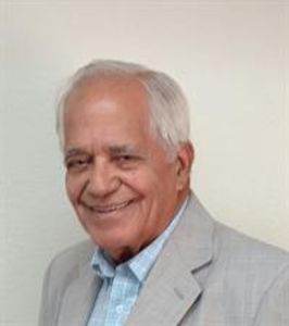 An older man in a suit smiling at the camera.