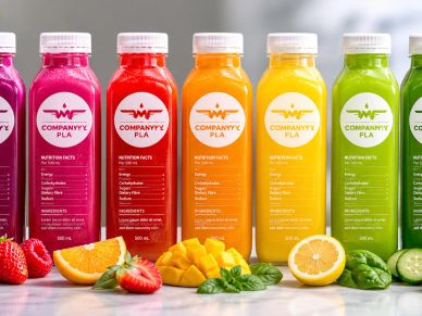 Colorful bottles of fresh fruit and vegetable juices lined up with fruits and greens.
