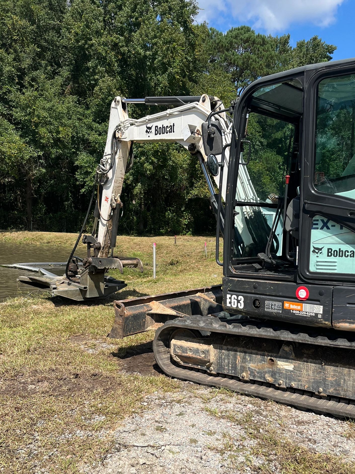 Mini Excavator with brush cutter attachment cleaning up the edges of a pond.