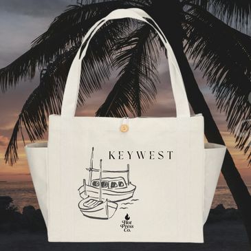 Cream tote bag with boat sketch and Key West text against a tropical sunset.