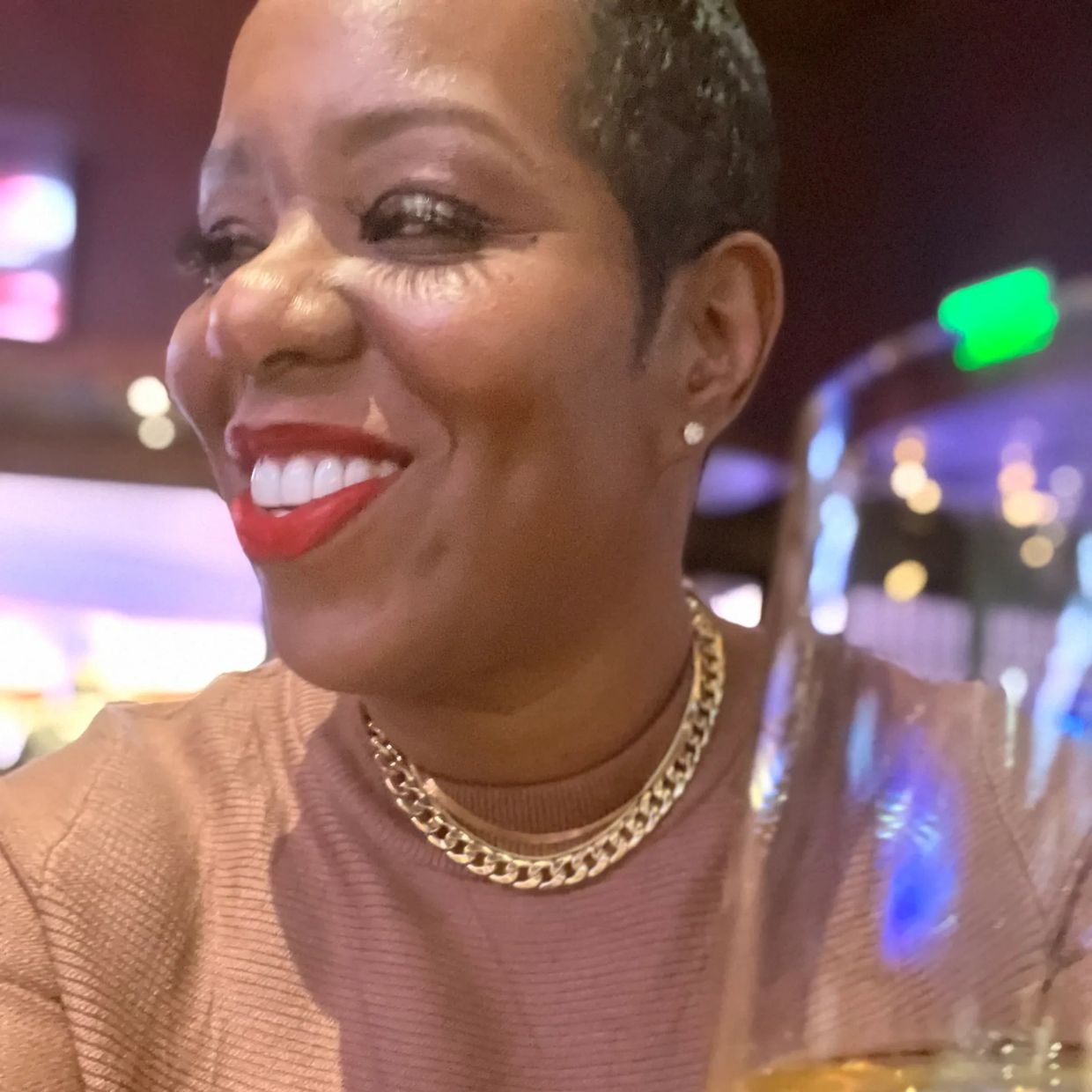 Woman smiling with bold red lipstick and gold chain necklace.