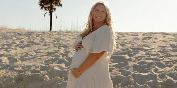 Pregnant woman smiling on a sandy beach at sunset.