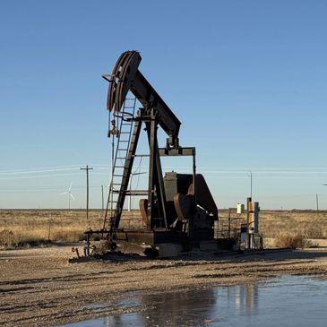 An oil pumpjack operating in a dry, open field under a clear blue sky.