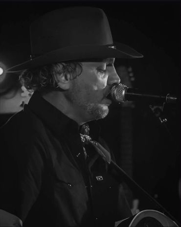 Zwarte-wit foto van een man die zingt met een hoed op.