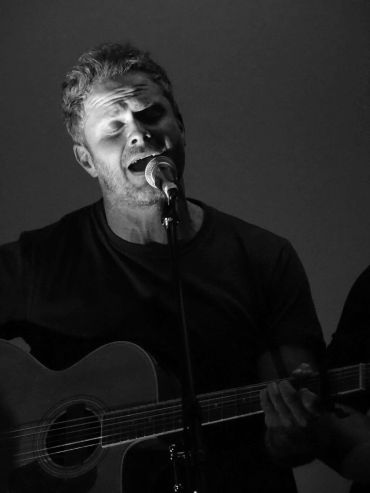 Zwart-wit foto van een man die gitaar speelt en zingt.