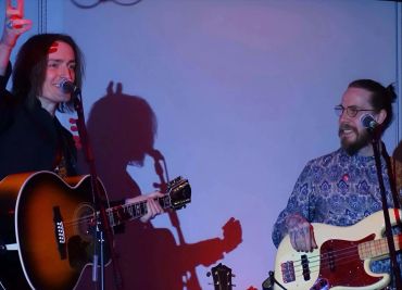 Twee muzikanten spelen gitaar en basgitaar op het podium.