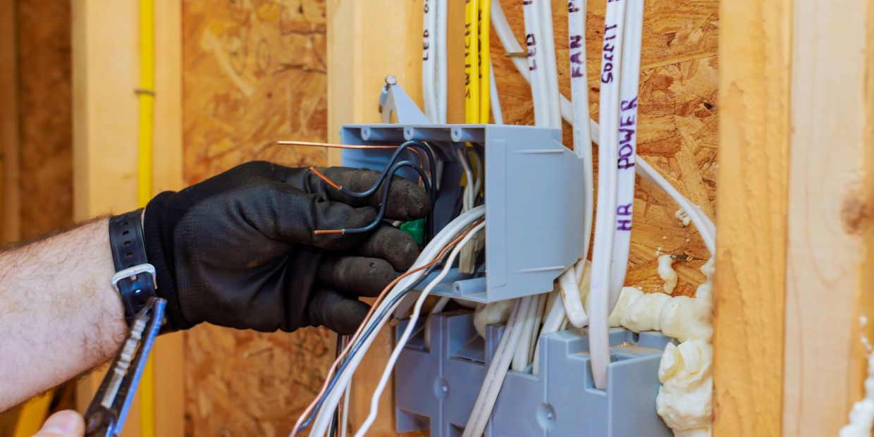 Electrician working on wiring inside a plastic electrical box in a wooden frame.