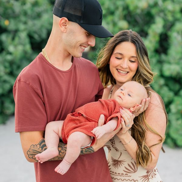Happy young couple holding their baby outdoors with greenery in background.