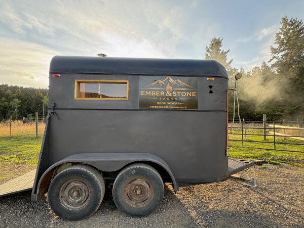 A black mobile sauna trailer with signage in a rural setting.