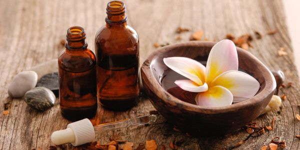 Spa setting with essential oils and a flower in a wooden bowl.