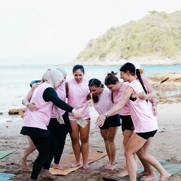 Group of women in pink shirts huddling on a beach.