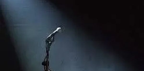 A microphone illuminated by a single spotlight on a dark stage.