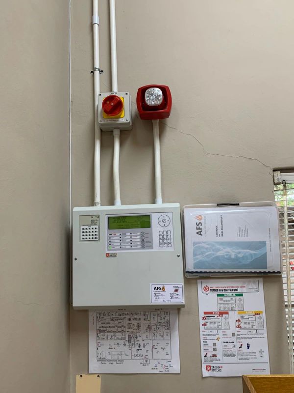 Fire alarm control panel mounted on a wall with documentation.