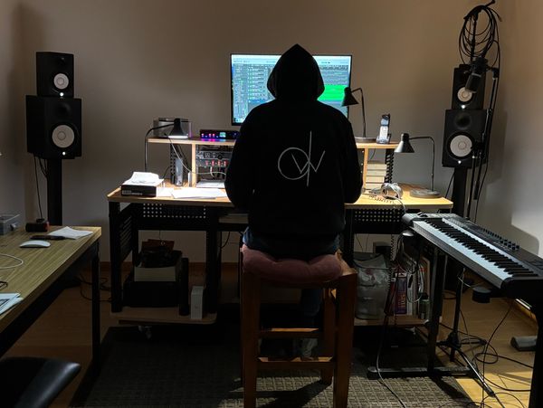 Person in a hoodie working on music production at a home studio desk.