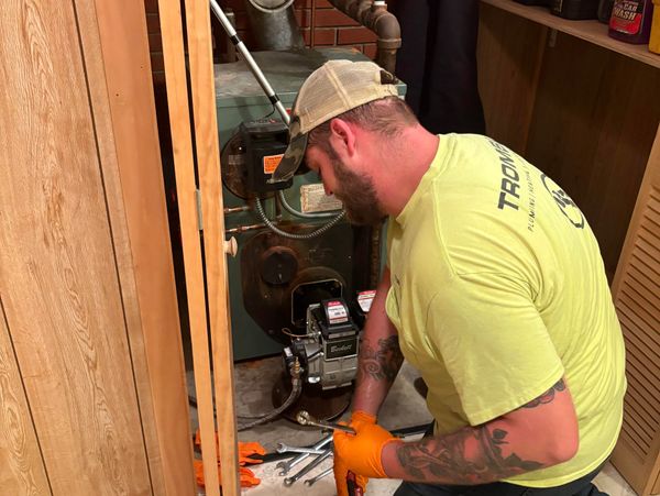 Technician repairing a furnace with tools and orange gloves.