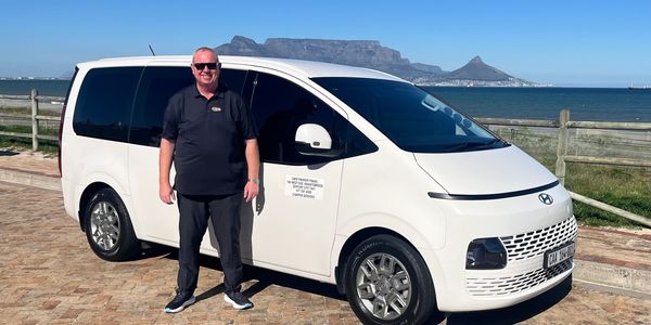 Man standing next to a white minivan with Table Mountain in the background.