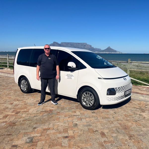Man standing next to a white minivan with Table Mountain in the background.