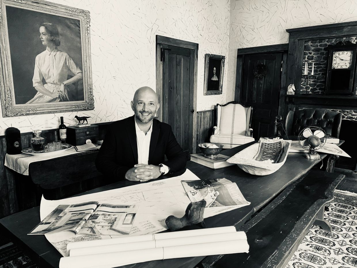 Man sitting at a desk with architectural plans in a vintage room.