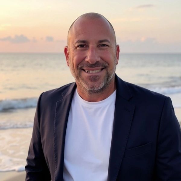 Smiling man in a blazer at the beach during sunset.