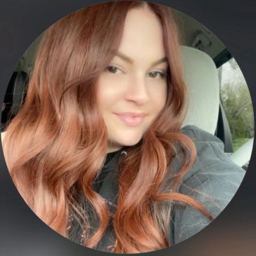 Young woman with long wavy red hair smiling inside a car.