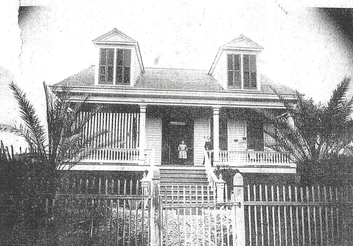 Black and white photo of a vintage house with a picket fence.