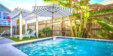 Backyard pool with umbrella and lounge chairs.