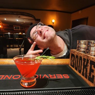 A man posing happily behind a red cocktail at a bar.