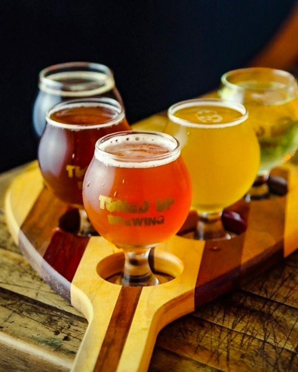 Flight of craft beers in varied colors on a wooden tray.