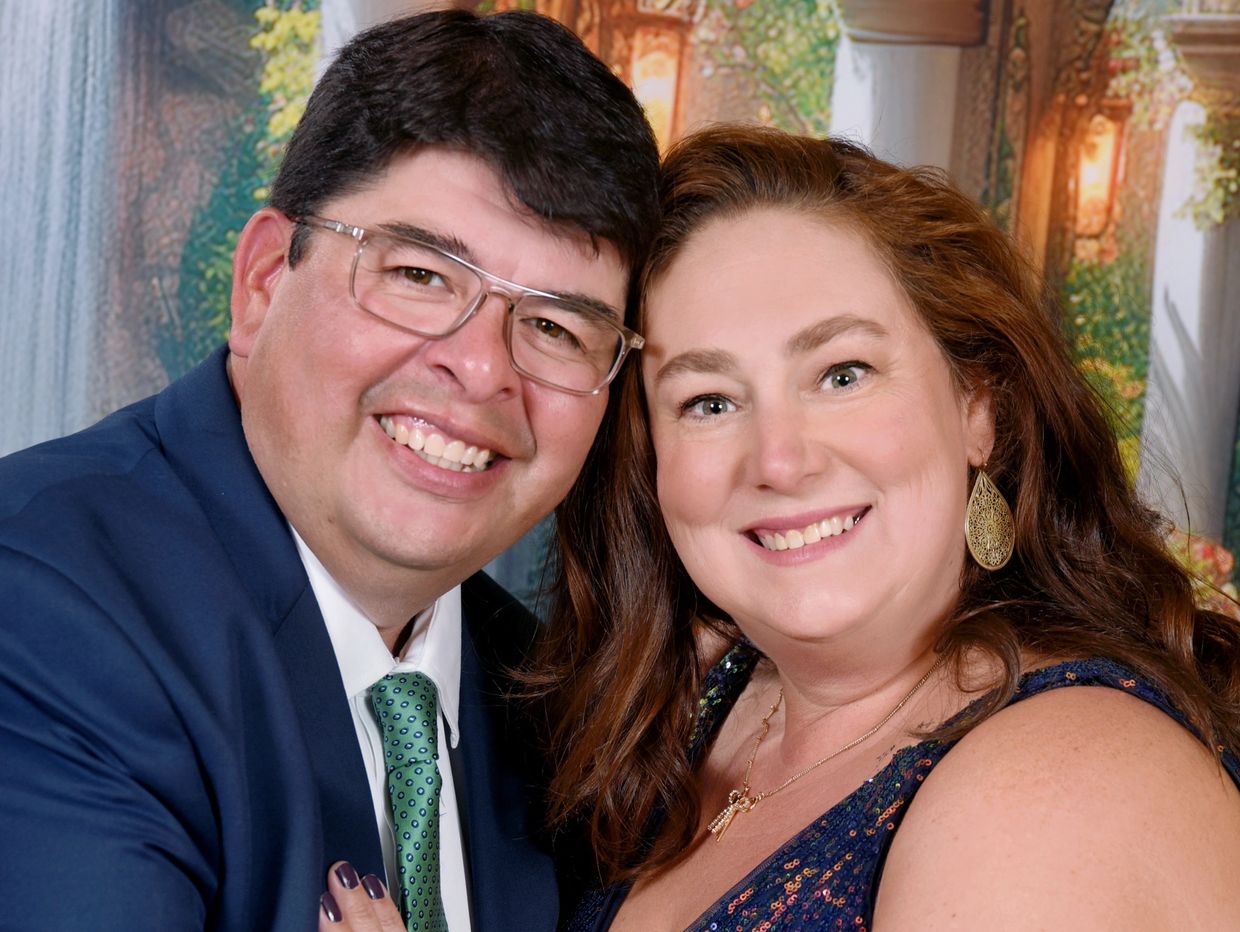 Smiling couple embracing each other in formal attire at a festive event.