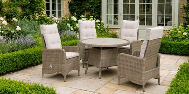 Outdoor patio set with round table and cushioned wicker chairs in garden.