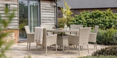 Outdoor dining set with six wicker chairs and a round table on a patio.