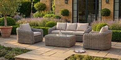 Outdoor patio set with wicker furniture and beige cushions on stone tiles.