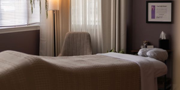 Cozy therapy room with a massage table, chair, and soft lighting.