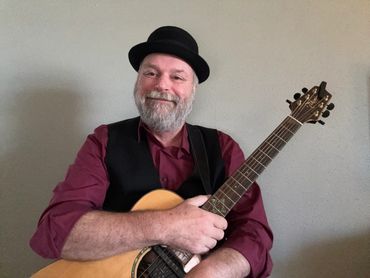 Smiling man in a hat holding an acoustic guitar.