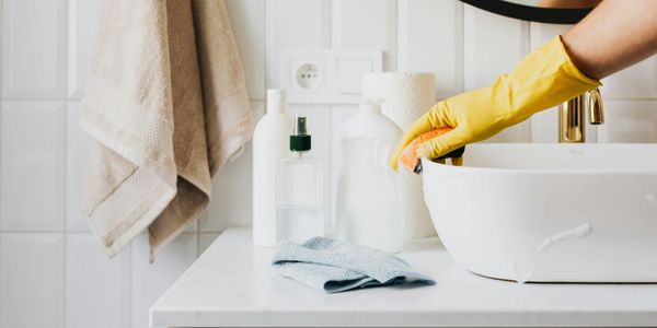 A hand in a yellow rubber glove cleaning a bathroom sink