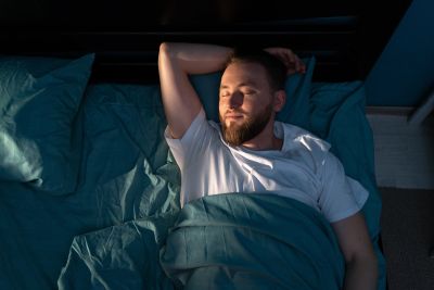 Man peacefully sleeping in bed under blue sheets.