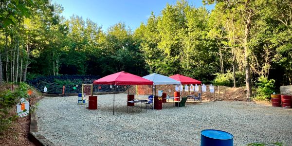 Outdoor shooting range setup with tents and targets in a forest clearing.
