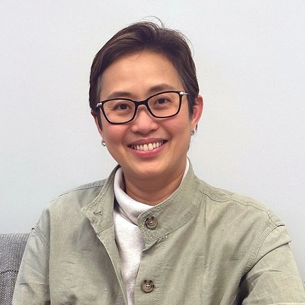 Smiling person with glasses wearing a light green jacket and white turtleneck.
