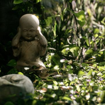 Small statue covering ears in leafy garden.
