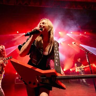Female rock musician performing with electric guitar on stage.