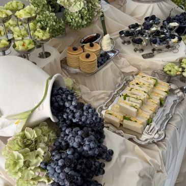Elegant table setting with grapes, sandwiches, and blueberries on white cloth.