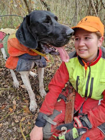 Hunter with dog wearing protective gear in the woods.