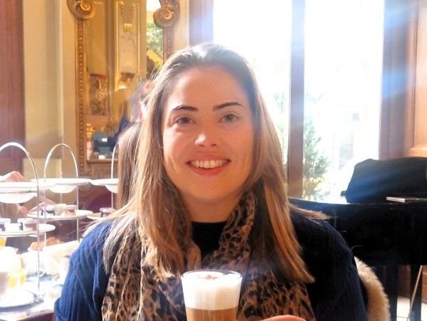 Smiling woman enjoying a latte in a cozy café with elegant decor.
