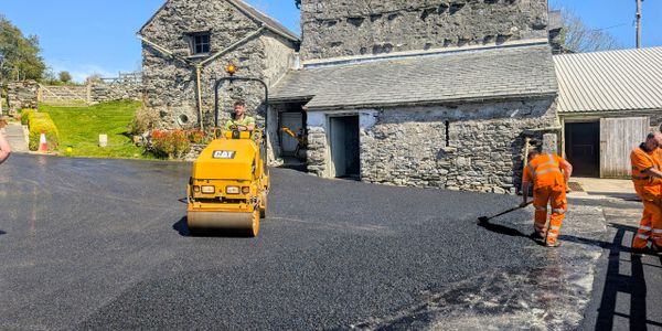 Workers laying asphalt near old stone buildings on a sunny day.