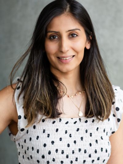 Smiling woman with long hair wearing a white polka dot top.