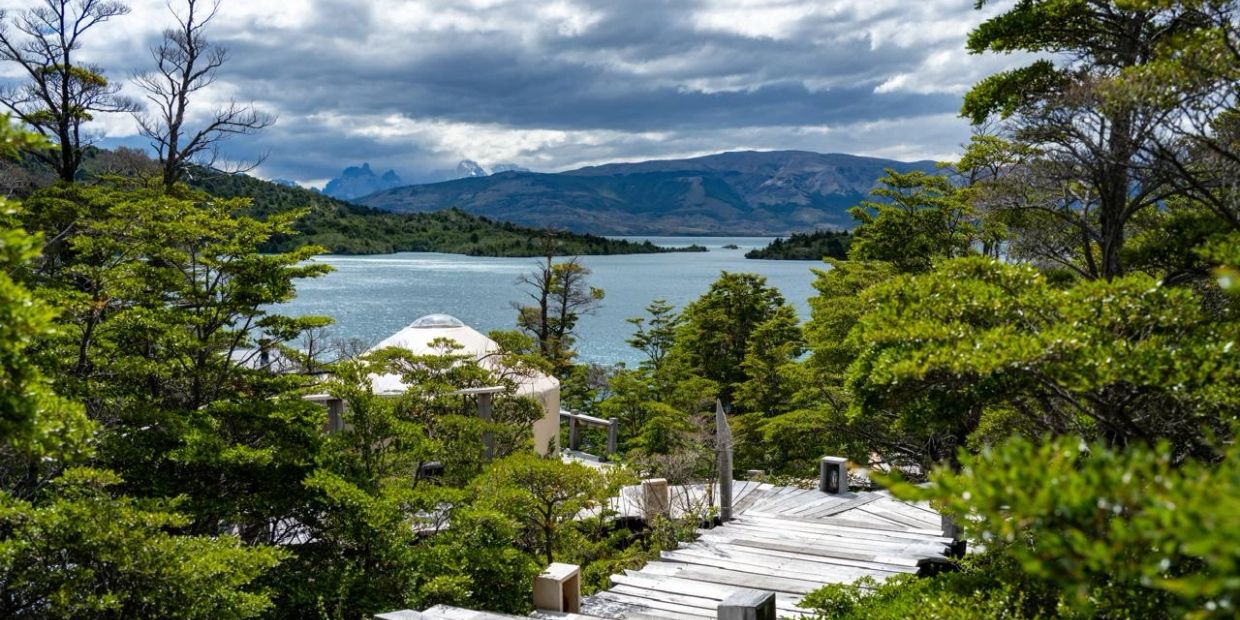 Scenic view of lake, mountains, and greenery with a wooden walkway.
