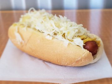 Little Kraut Doggie all-beef hot dog on plain bun with spicy mustard and hot sauerkraut on table