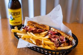 Pastrami sandwich in a basket with french fries, with a cold Pacifico beer.