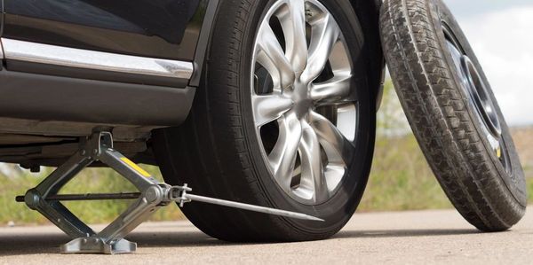 Car tire being changed with a jack and spare tire on the side.